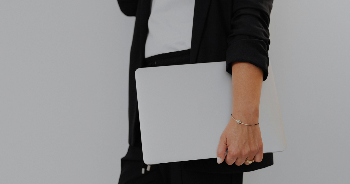 Female in black blazer and trousers with white tank top holding a computer.