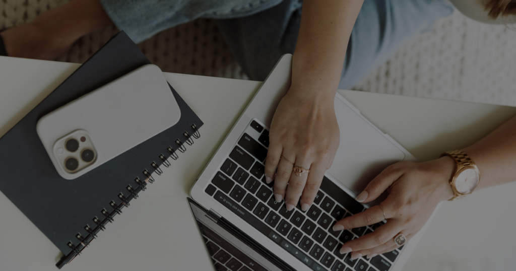 Female hands typing on a laptop with a phone social media explaining why your social media isn't generating leads from Up After Studios